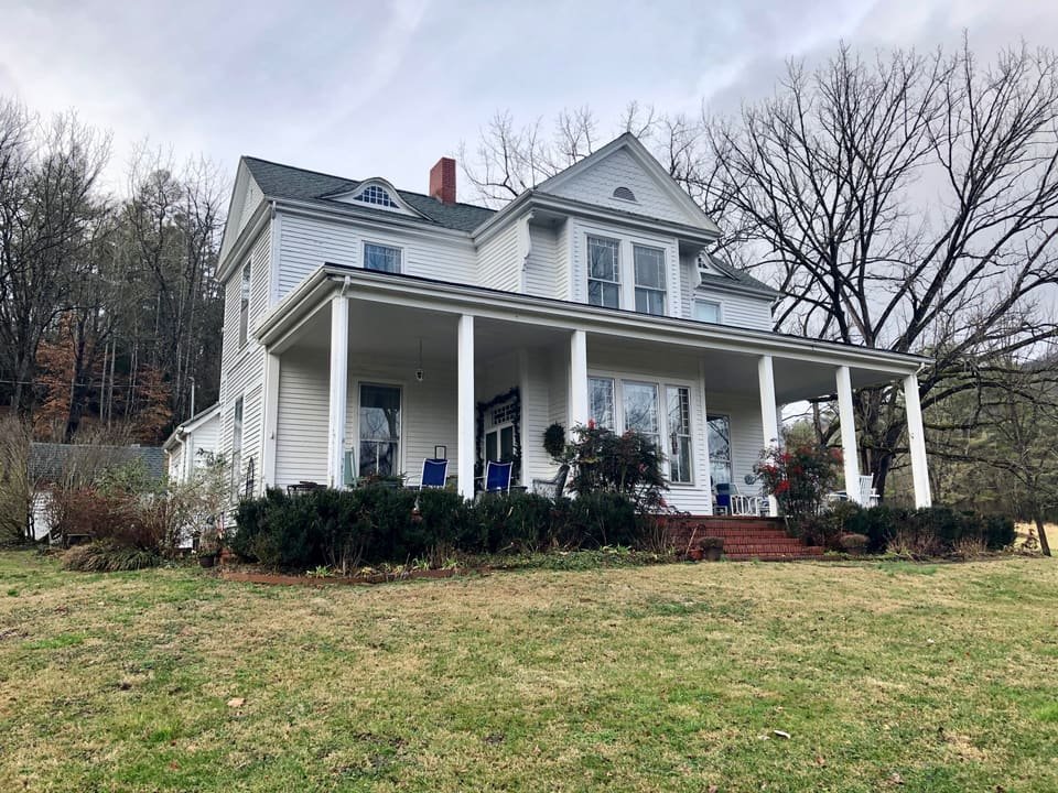 A white two-storey house with a long front porch and a green lawn