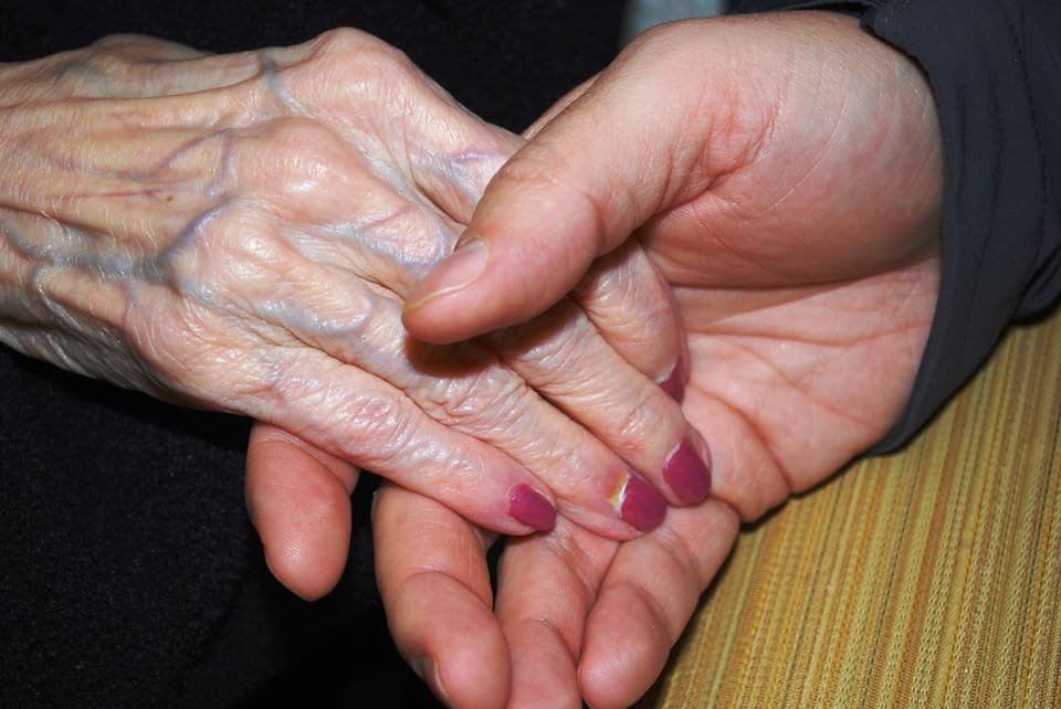 A younger hand gently holding an older person's hand